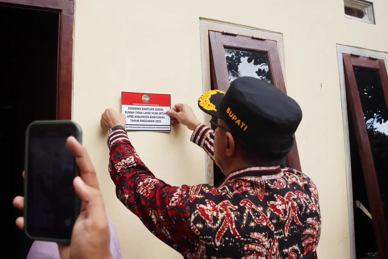 Bupati Banyumas Sadewo Tri Lastiono menempelkan stiker di tembok rumah warga yang menerima bantuan renovasi RTLH, sebagai simbolis penyerahan rumah yang telah di renovasi, Rabu (12/11/2025).