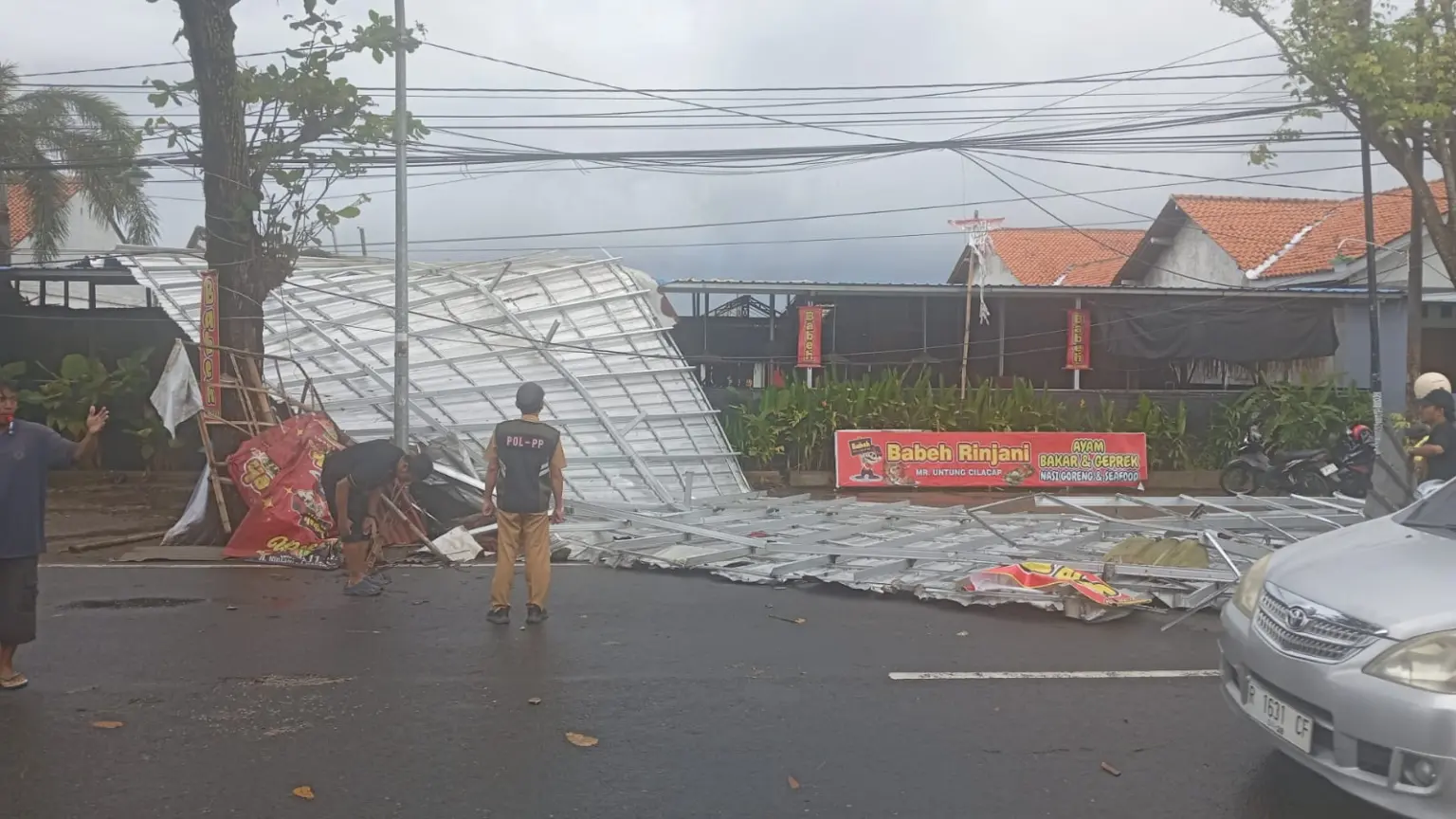 Petugas dan warga saat evakuasi atap rumah makan yang terbang ke jalan akibat hujan dan angin kencang. (BPBD Cilacap).